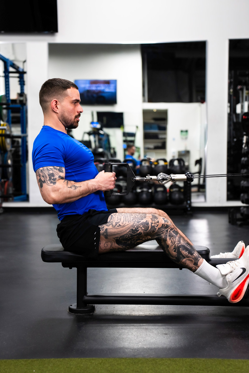 The coach performing a lat pulldown while wearing white over-ear headphones in a dark gym setting.