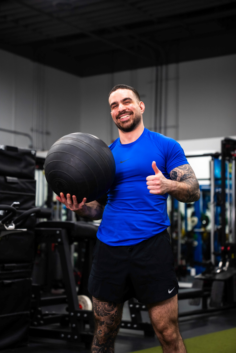 The coach performing an L-sit hold on a kettlebell in a dimly lit gym.
